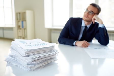 Stack of documents on the desk and pensive male employee working on background